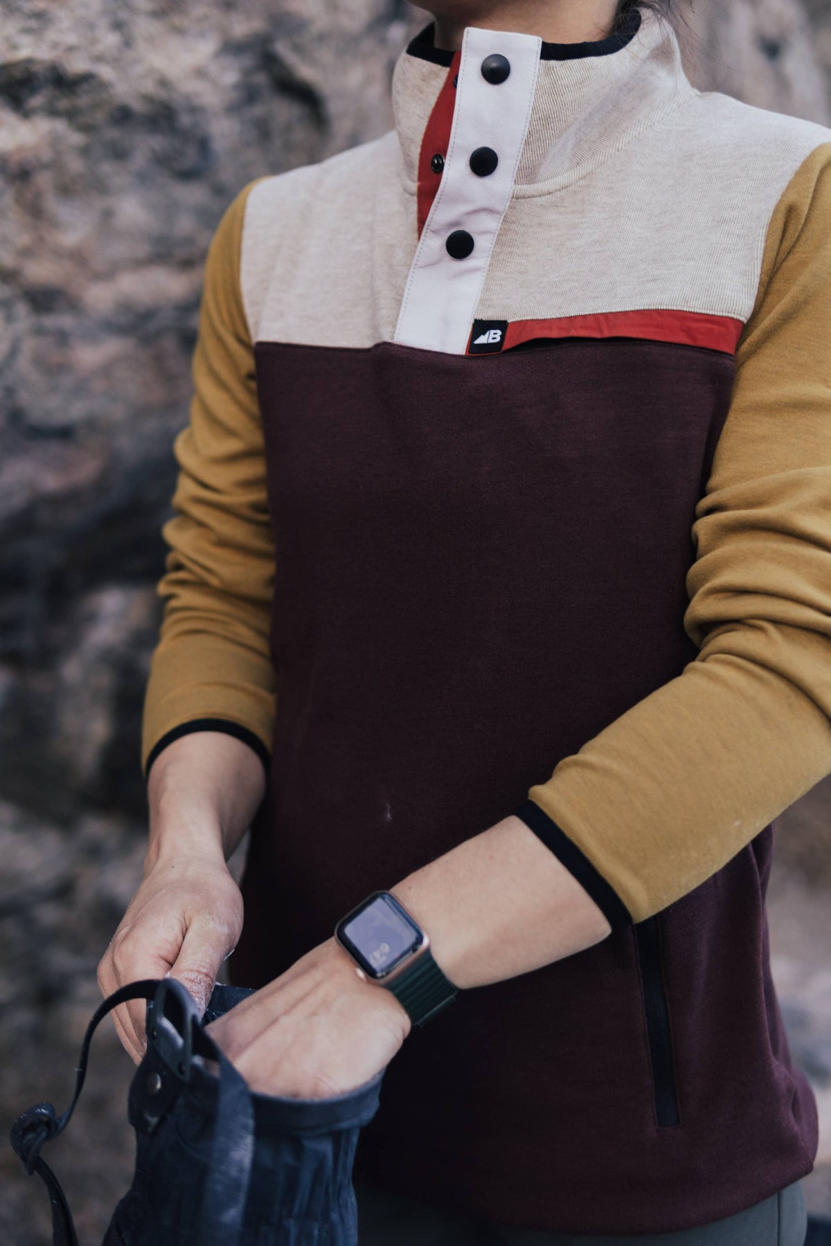 Person wearing a two-tone shirt with a maroon and beige design, holding a phone.