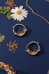 Gold hoop earrings with gemstones on a blue background with floral elements