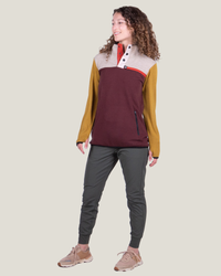 Woman wearing a colorful pullover with maroon, yellow, and gray sections on a beige background