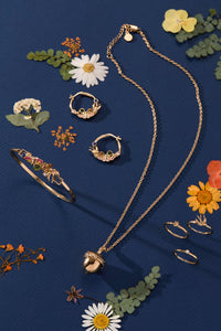 Gold jewelry including necklace, rings, and headband on a blue background with flowers.