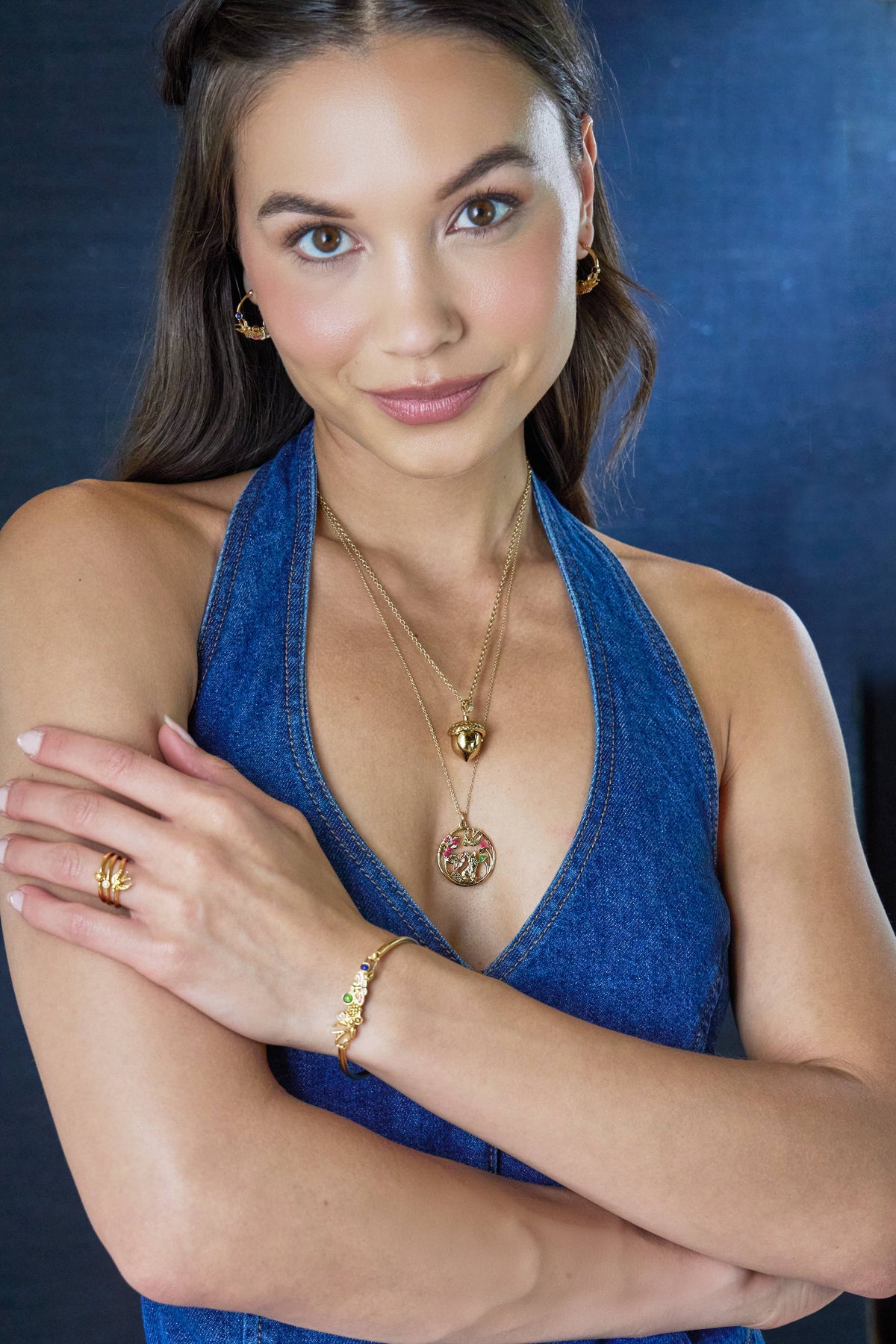 Woman wearing a blue dress with gold jewelry against a dark background