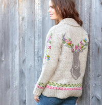 Woman wearing a floral embroidered sweater against a wooden fence.