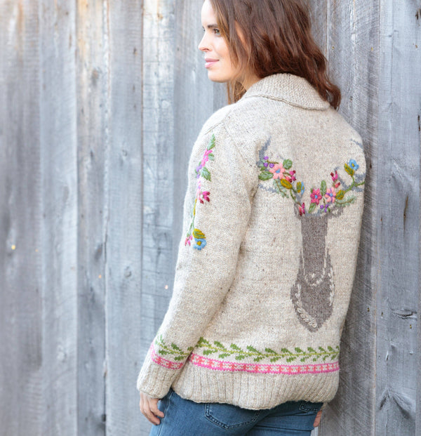 Woman wearing a floral embroidered sweater against a wooden fence.