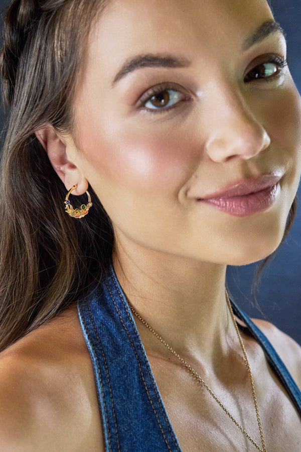 Close-up of a woman wearing gold hoop earrings and a necklace against a blue background