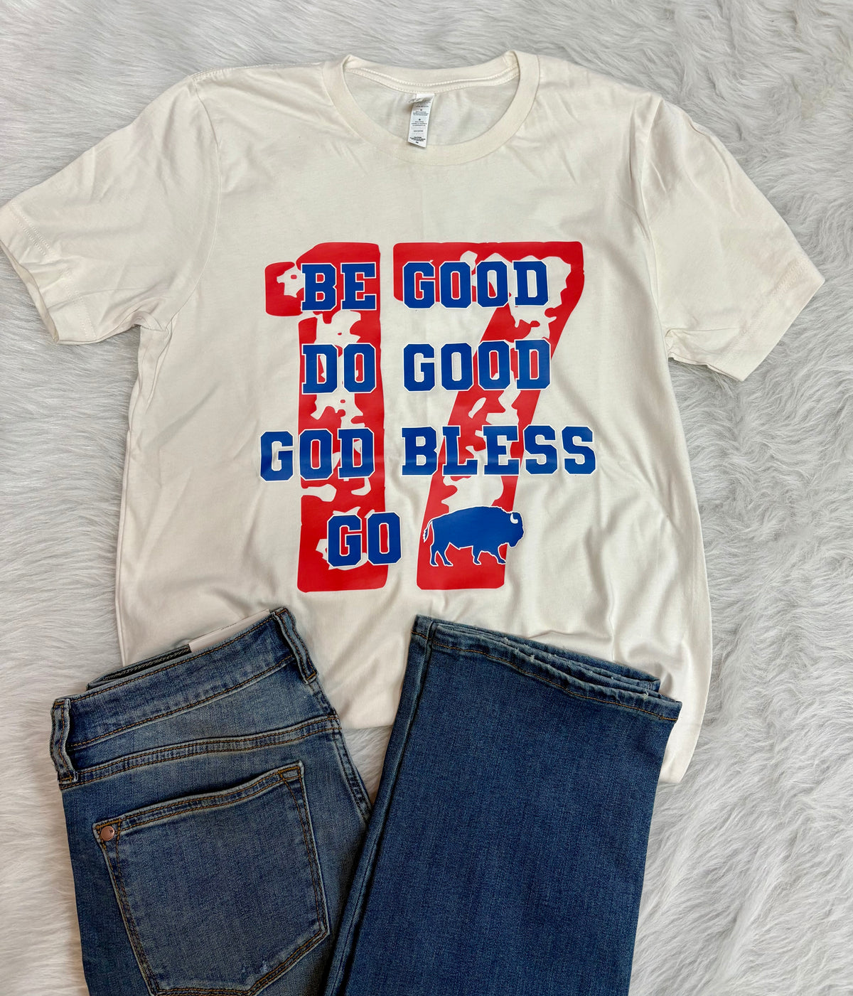 White t-shirt with red and blue graphic design on a gray surface with jeans.