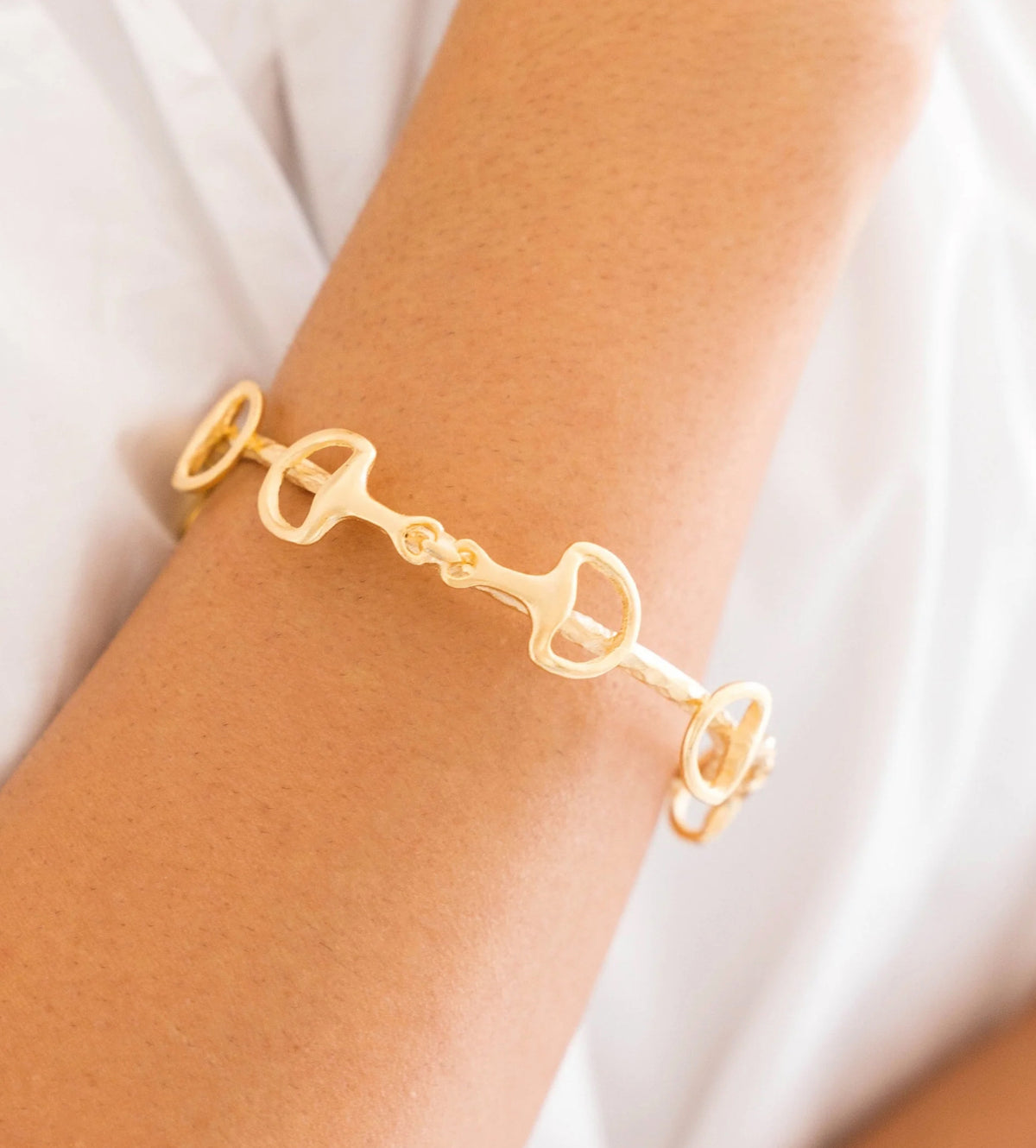 Gold bracelet on a wrist with a plain background