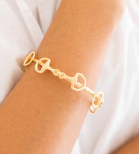Gold bracelet on a wrist with a plain background