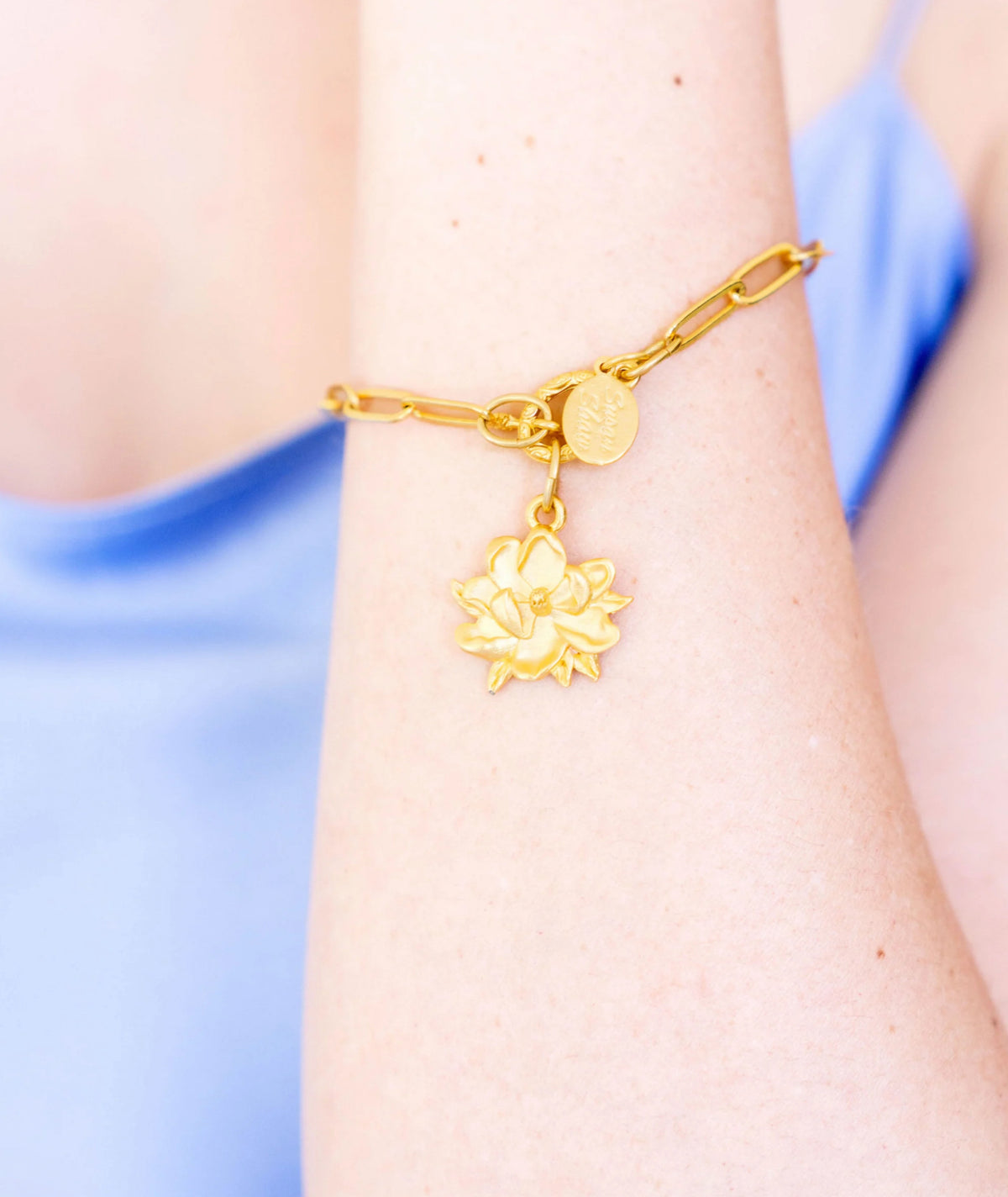 Gold bracelet with a lotus flower charm on a wrist against a blurred background