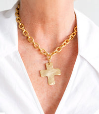 Gold chain necklace with a cross pendant on a white shirt background