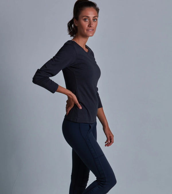 Woman wearing a dark blue long-sleeve top and pants against a gray background