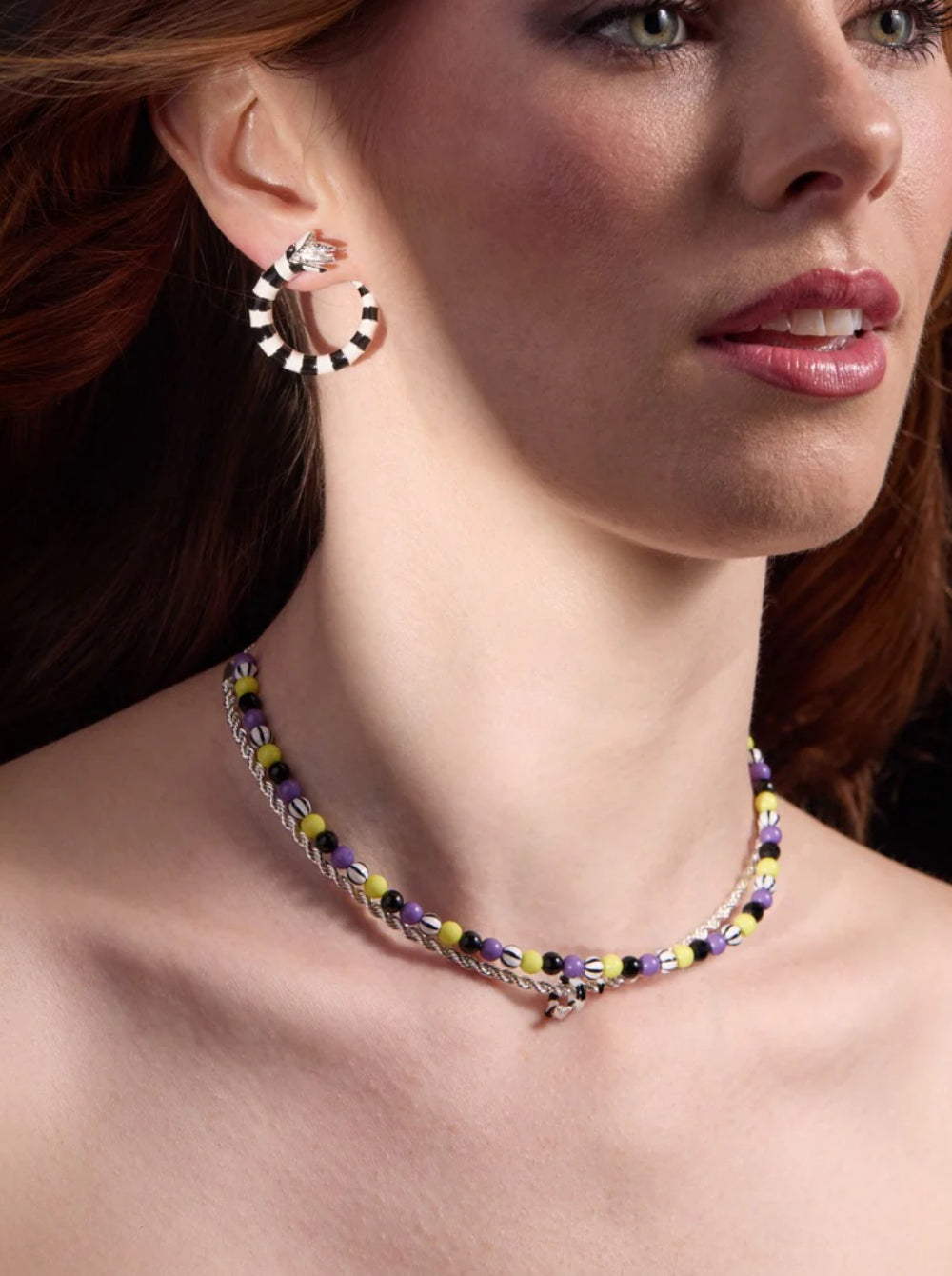 Close-up of a woman wearing a colorful beaded necklace and hoop earrings.