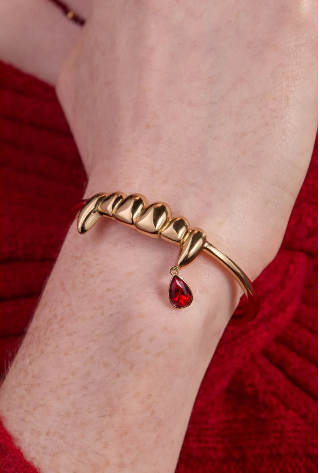 Gold bracelet with a red gemstone on a wrist against a red background