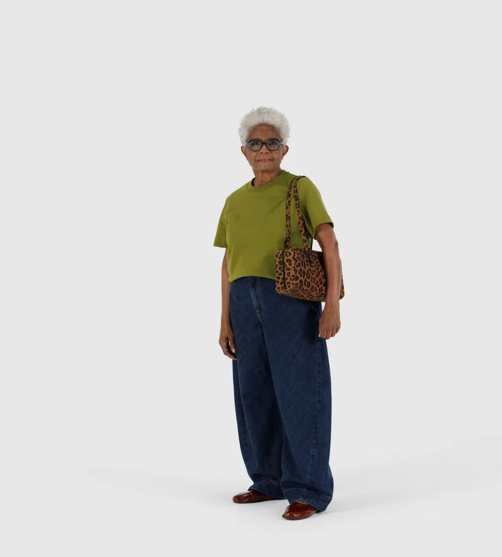 Woman wearing a green shirt and blue pants holding a leopard print bag on a white background