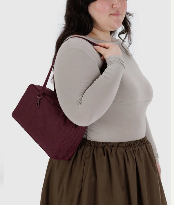 Woman wearing a gray long-sleeve top and brown skirt, holding a maroon handbag against a white background