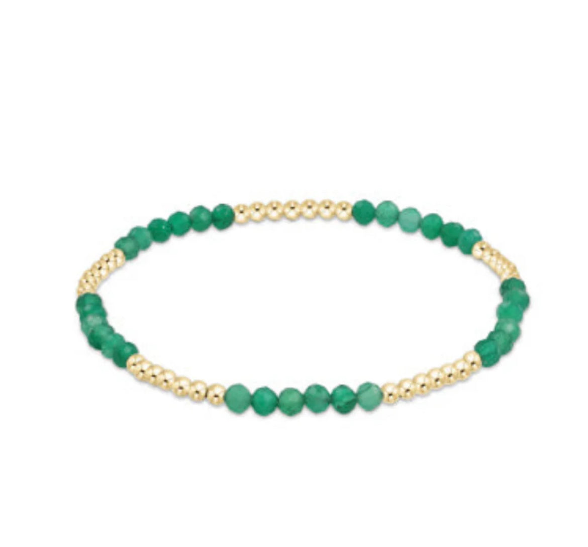 Green beaded bracelet with gold accents on a white background