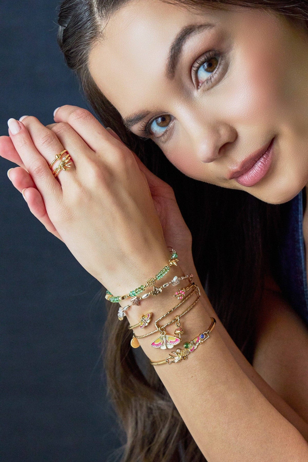 Woman wearing multiple bracelets and a ring on a dark background